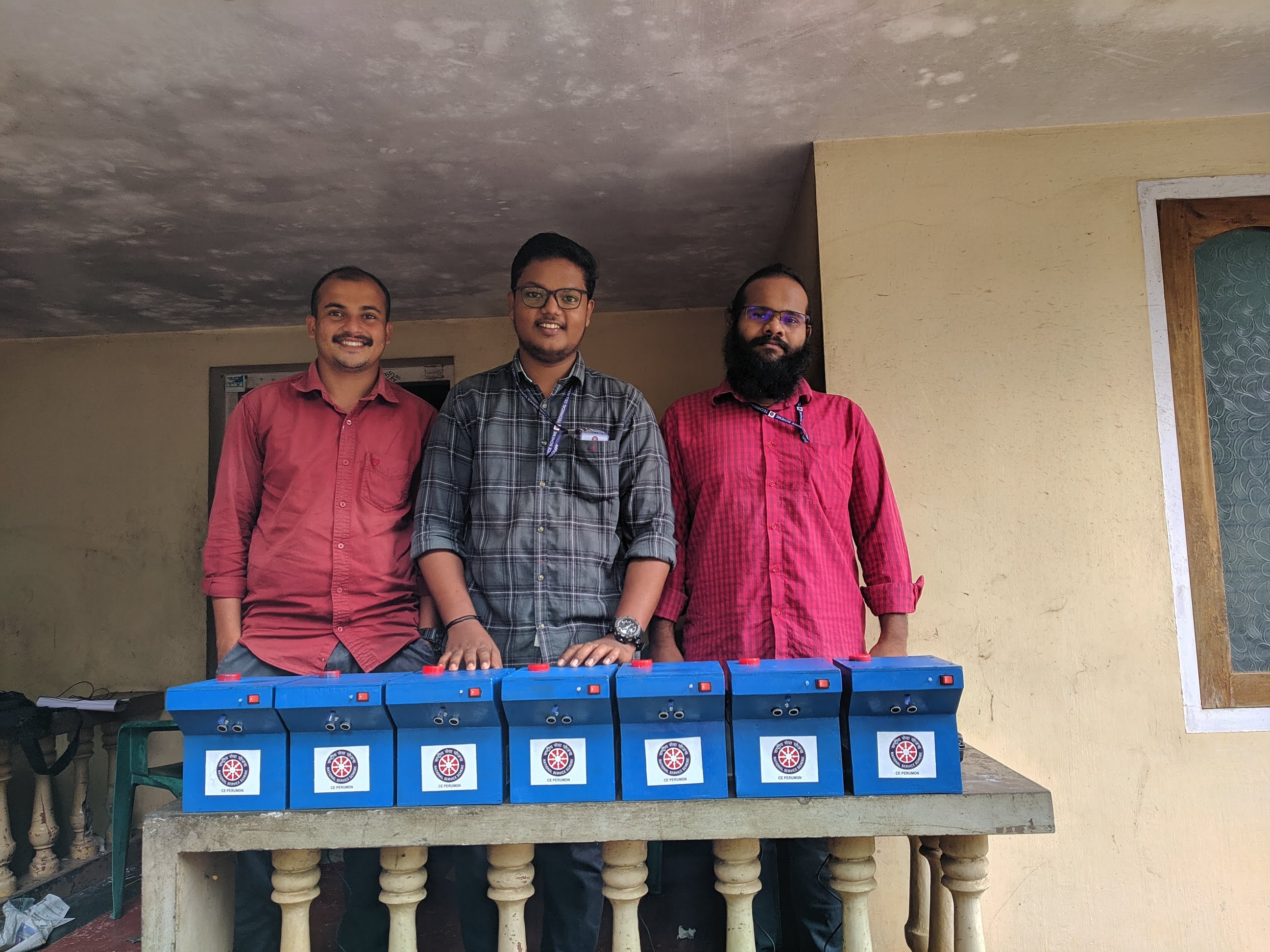Row of finished blue dispenser units on the porch of the campus building, awaiting placement at the panchayath treatment centre.